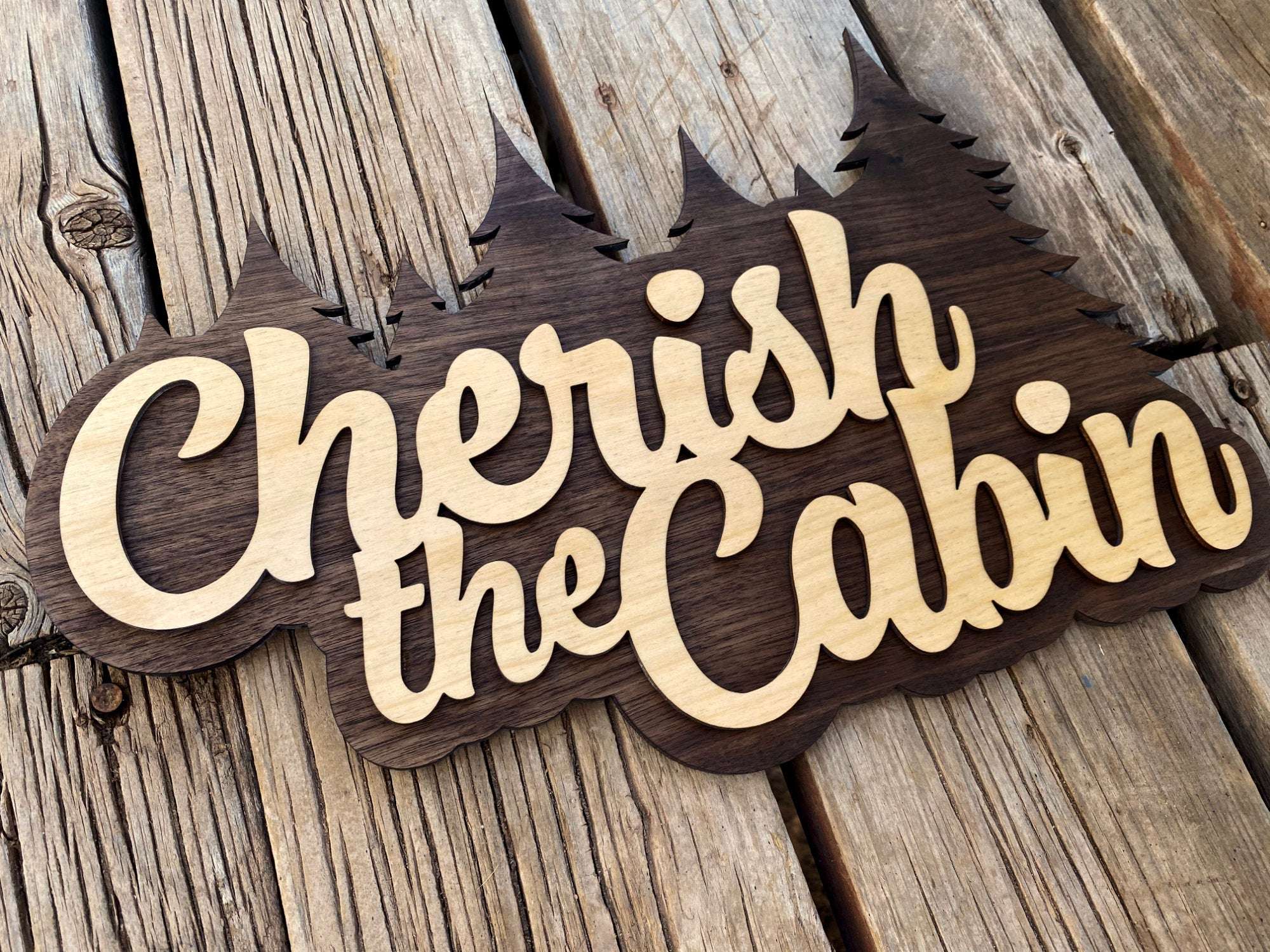 Wooden Cherish the Cabin wall art on rustic deck, ideal for home or cabin decor with Seinfeld-inspired charm.