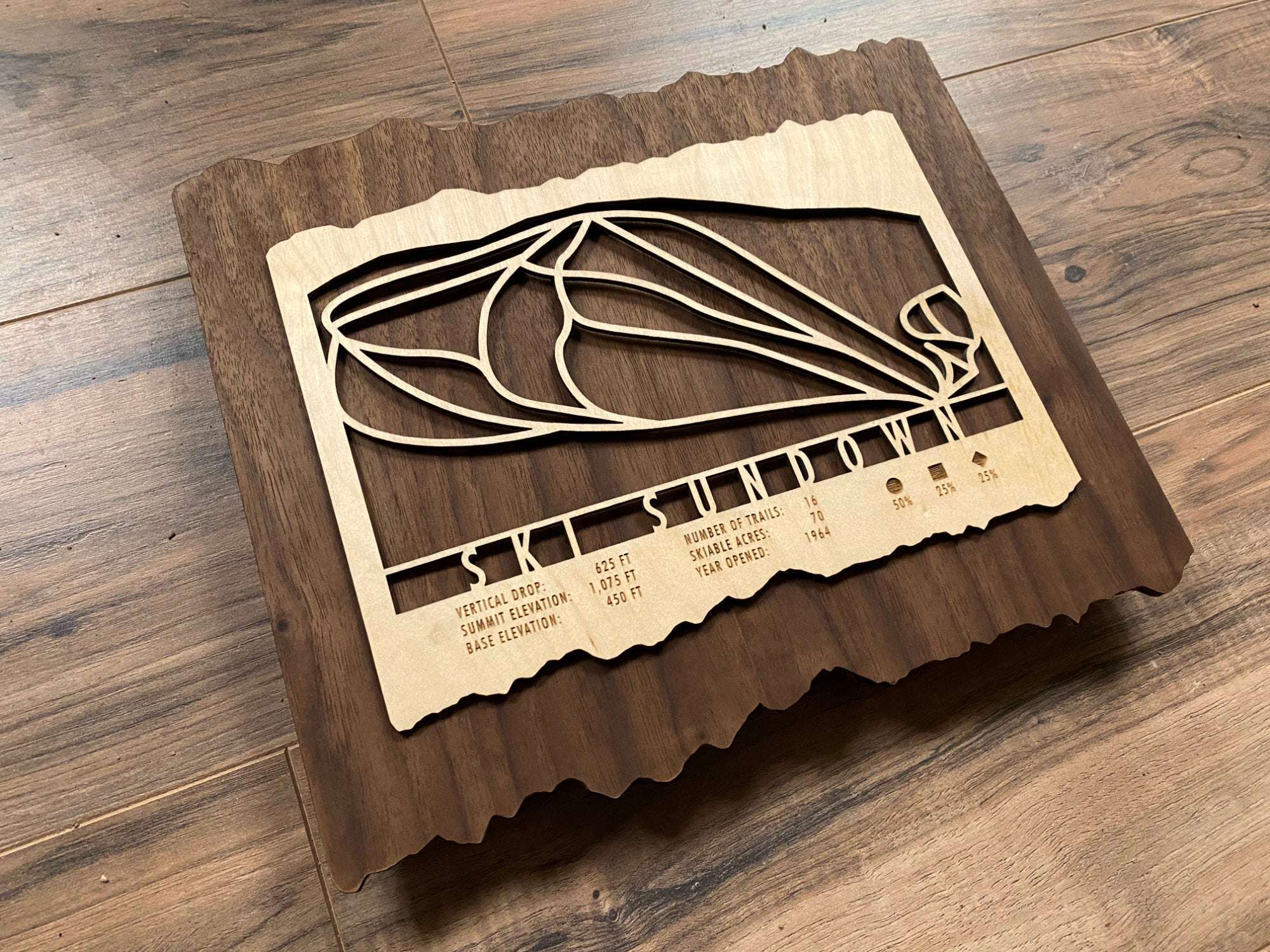 Angled view of Ski Sundown ski trail map carved in wood, showcasing detailed trail lines and engraved resort information on a dark wood background.