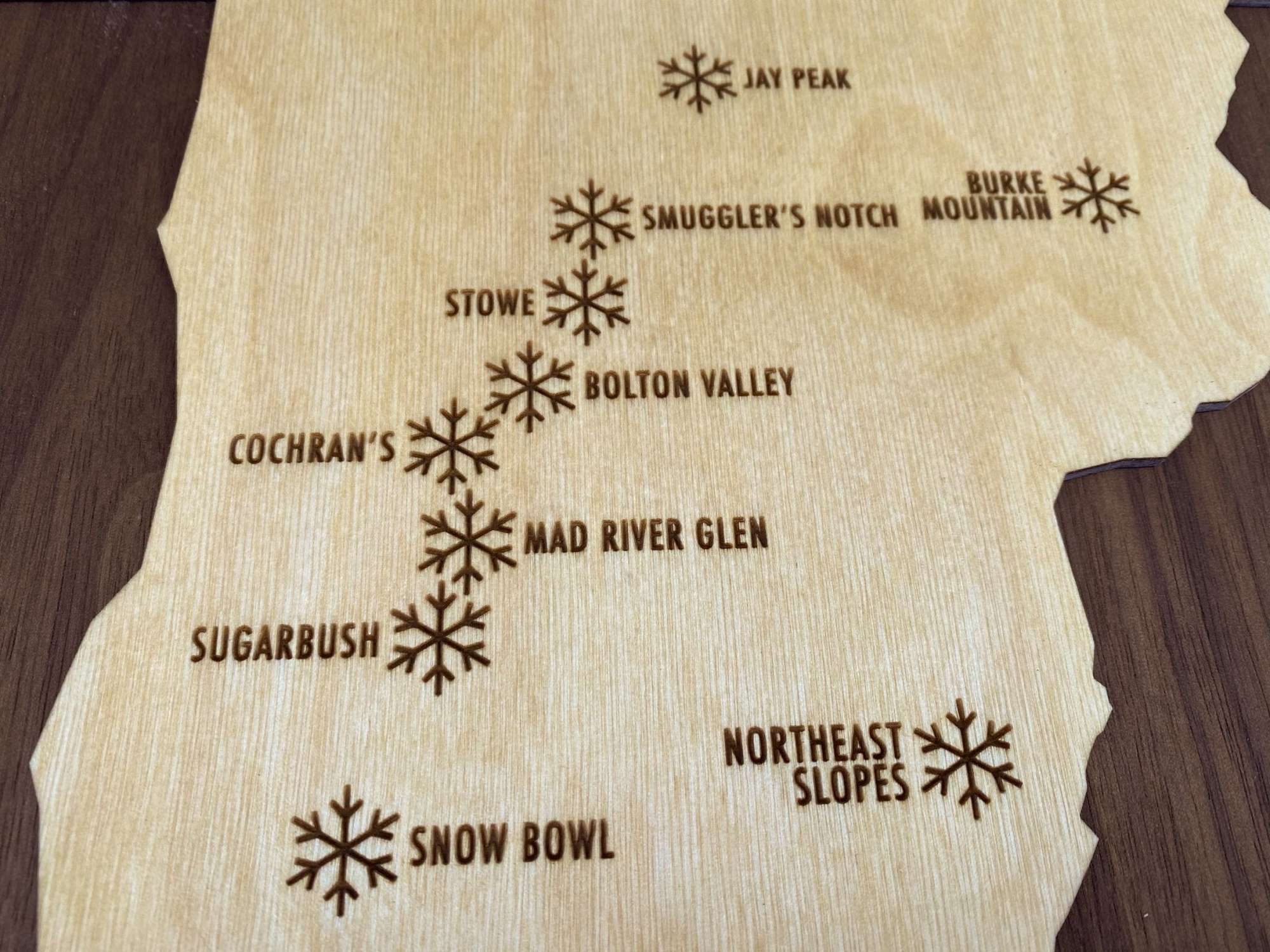 Detailed view of northern Vermont ski resorts engraved on wood decor, including Jay Peak and Stowe.