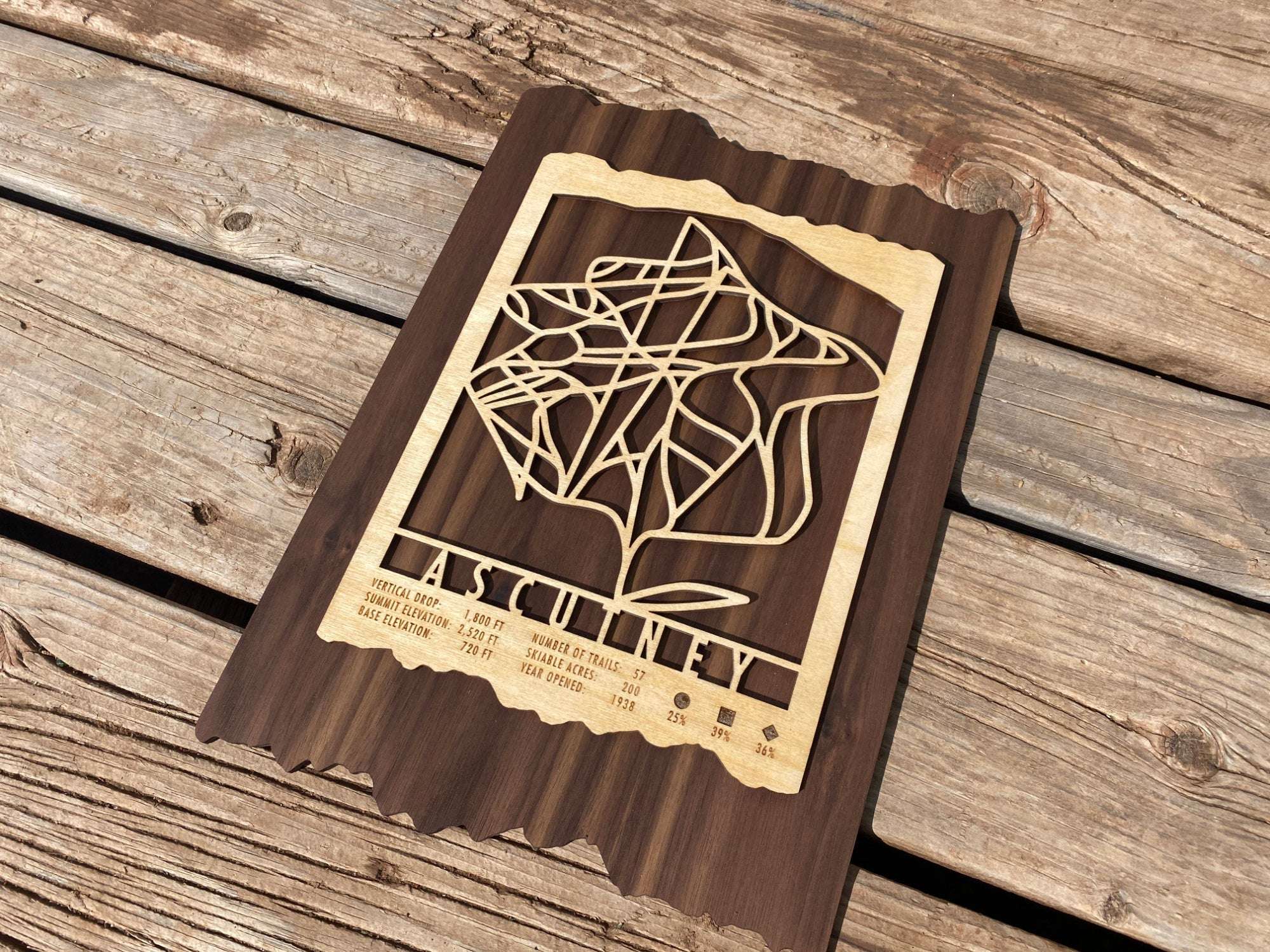 Wooden Ascutney Ski Trail Map decor placed on a wooden surface, showcasing detailed ski runs and engraved mountain stats for home or cabin display.