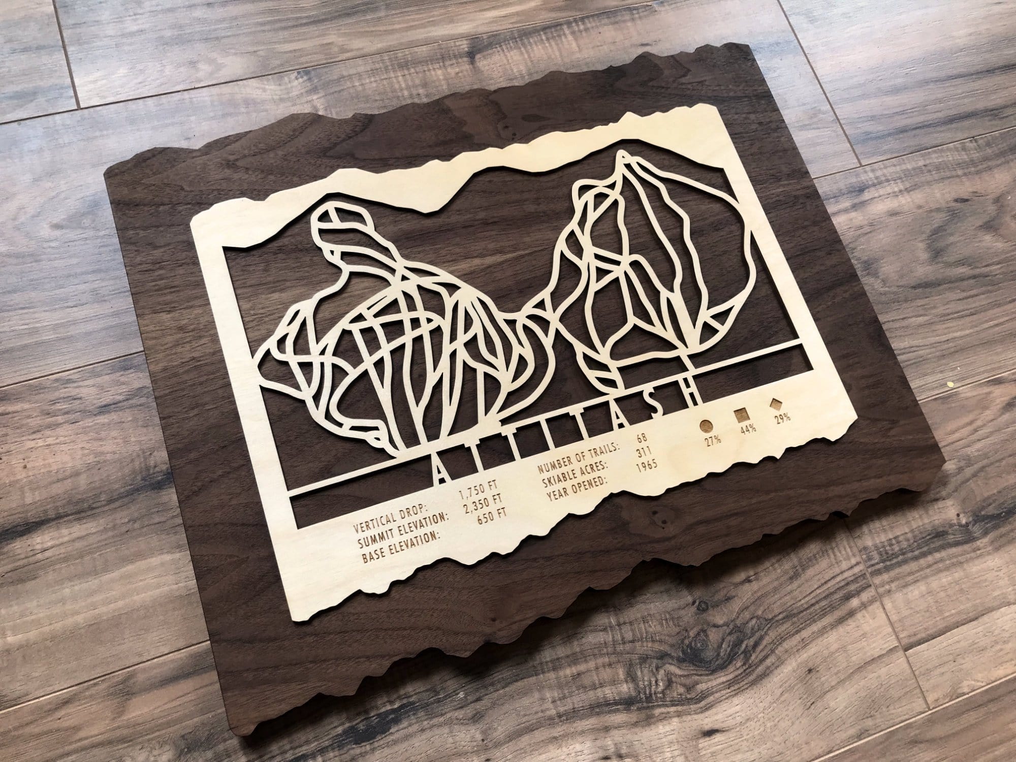 Wooden Attitash ski trail map decor on rustic floor, showcasing detailed ski runs and mountain stats for home or office ski-themed artwork.