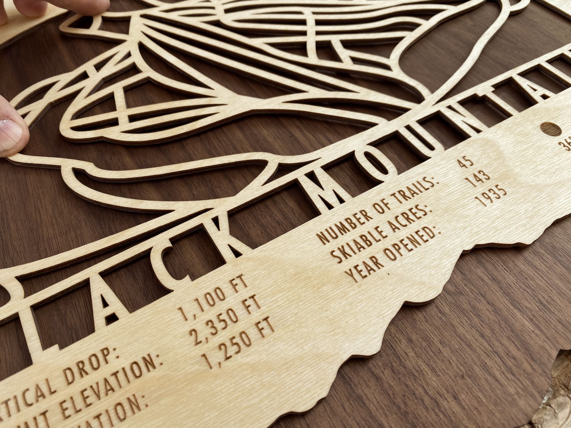 Black Mountain Trail Map - Wood Wall Decor - close-up of engraved ski trail names and resort stats on wood decor, ideal for ski-themed interiors.