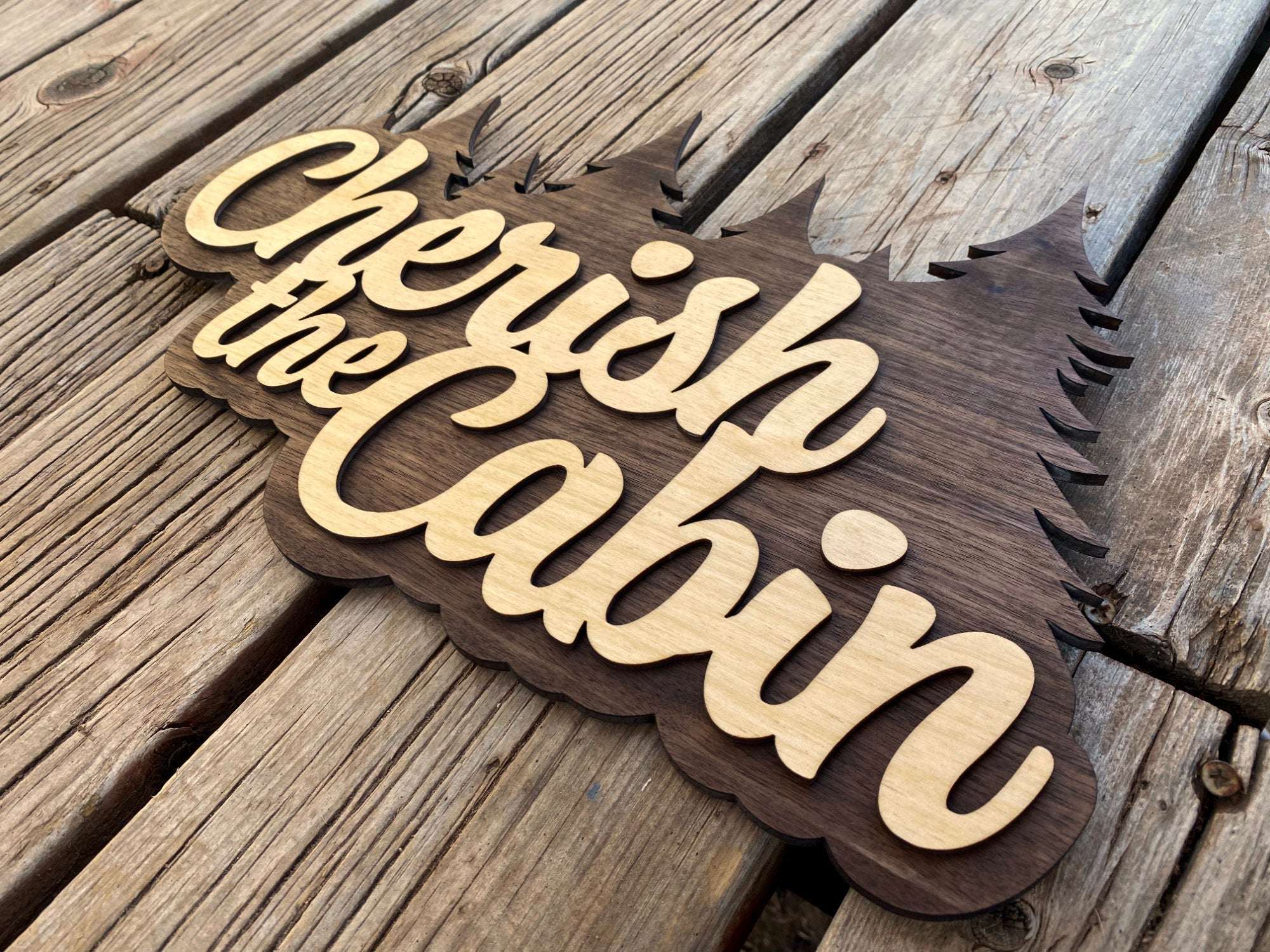 Angled view of Cherish the Cabin wooden wall sign with layered lettering and pine tree cutout, great for rustic interiors.