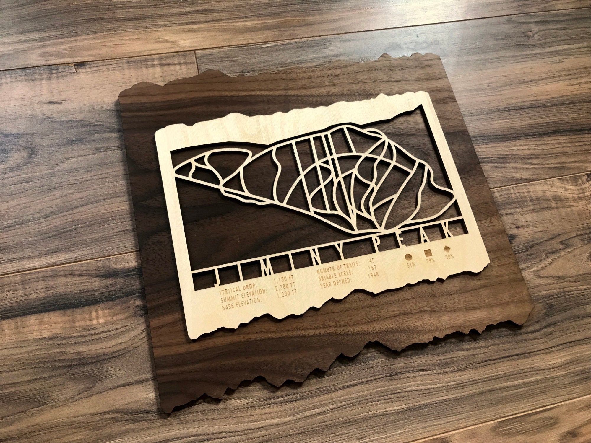 Angled view of Jiminy Peak Ski Trail Map - Wood Wall Decor - Mountaincut on hardwood floor, showcasing layered wood craftsmanship and ski trail design.