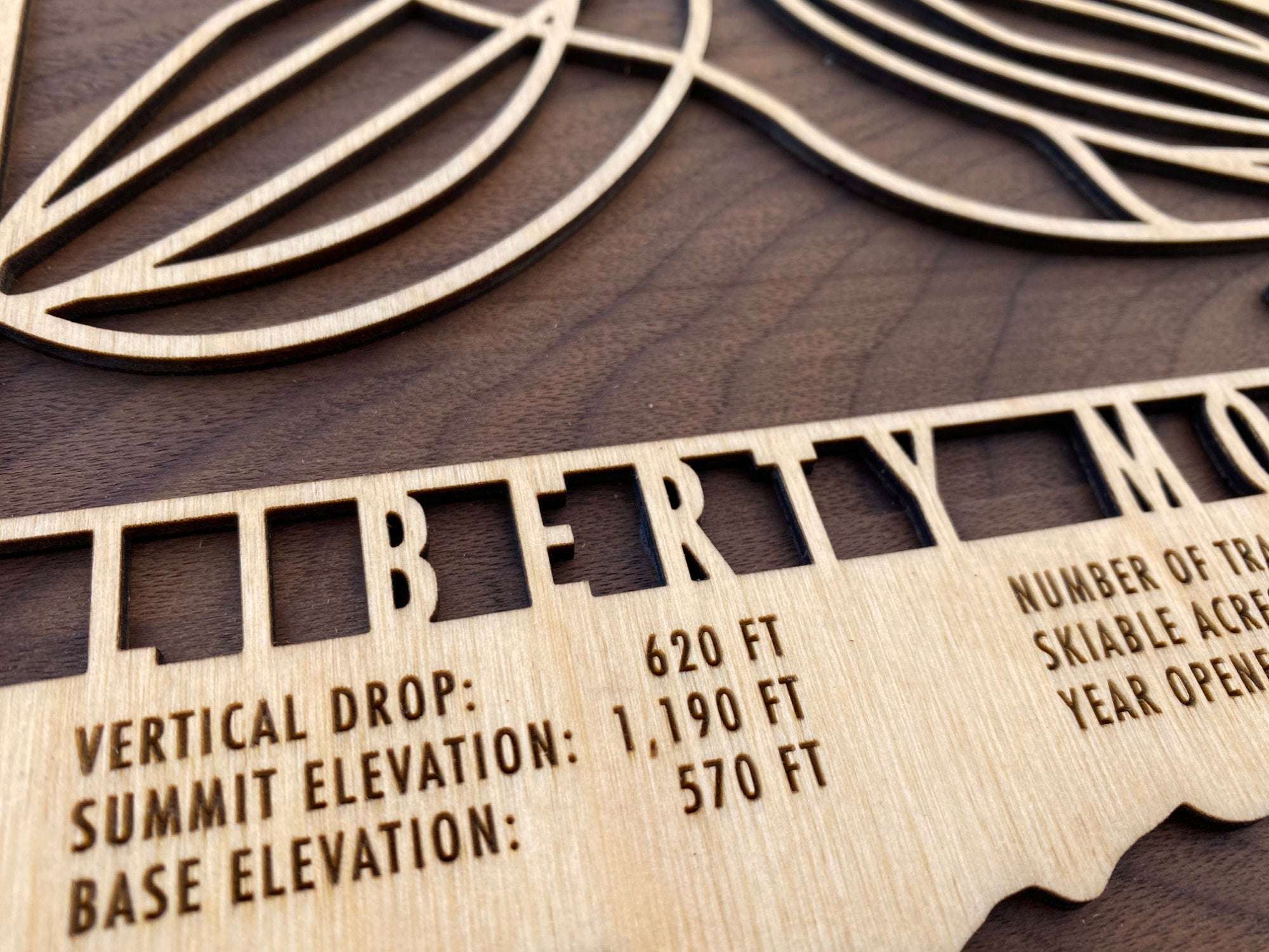 Close-up of Liberty Mountain wood ski map showing engraved resort stats including vertical drop, summit elevation, and trail count.