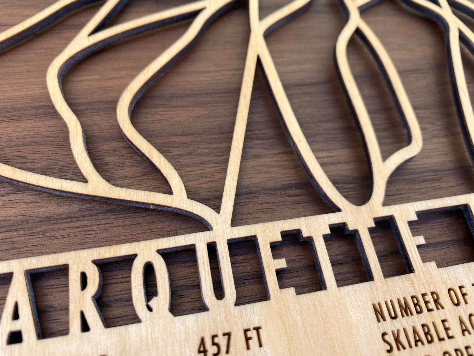 Close-up of Marquette Mountain wood ski map showing precision laser-cut lettering and trail design on natural wood grain background.