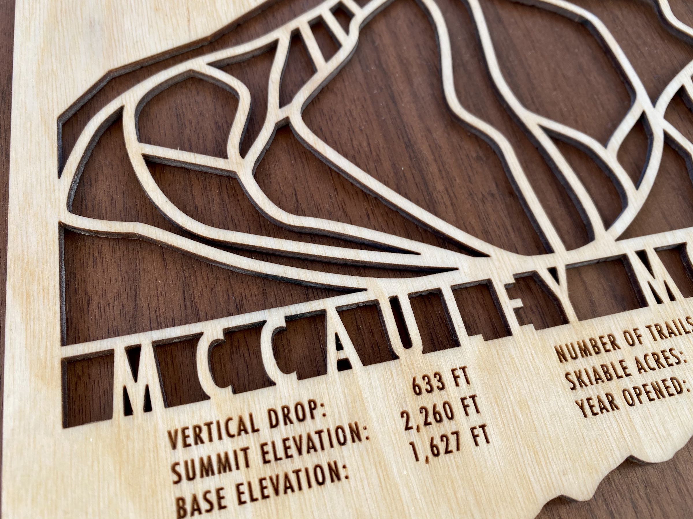 Close-up of McCauley Mountain wood ski map showing engraved elevation and trail data, handcrafted decor for ski enthusiasts.
