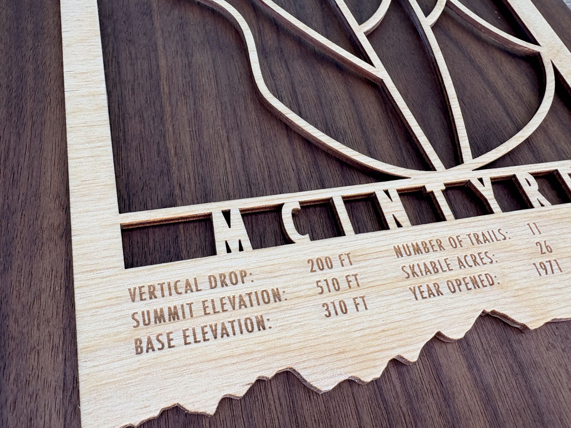 Detailed close-up of McIntyre Ski Area wooden trail map highlighting engraved vertical drop, elevation, and ski trail information on natural wood.