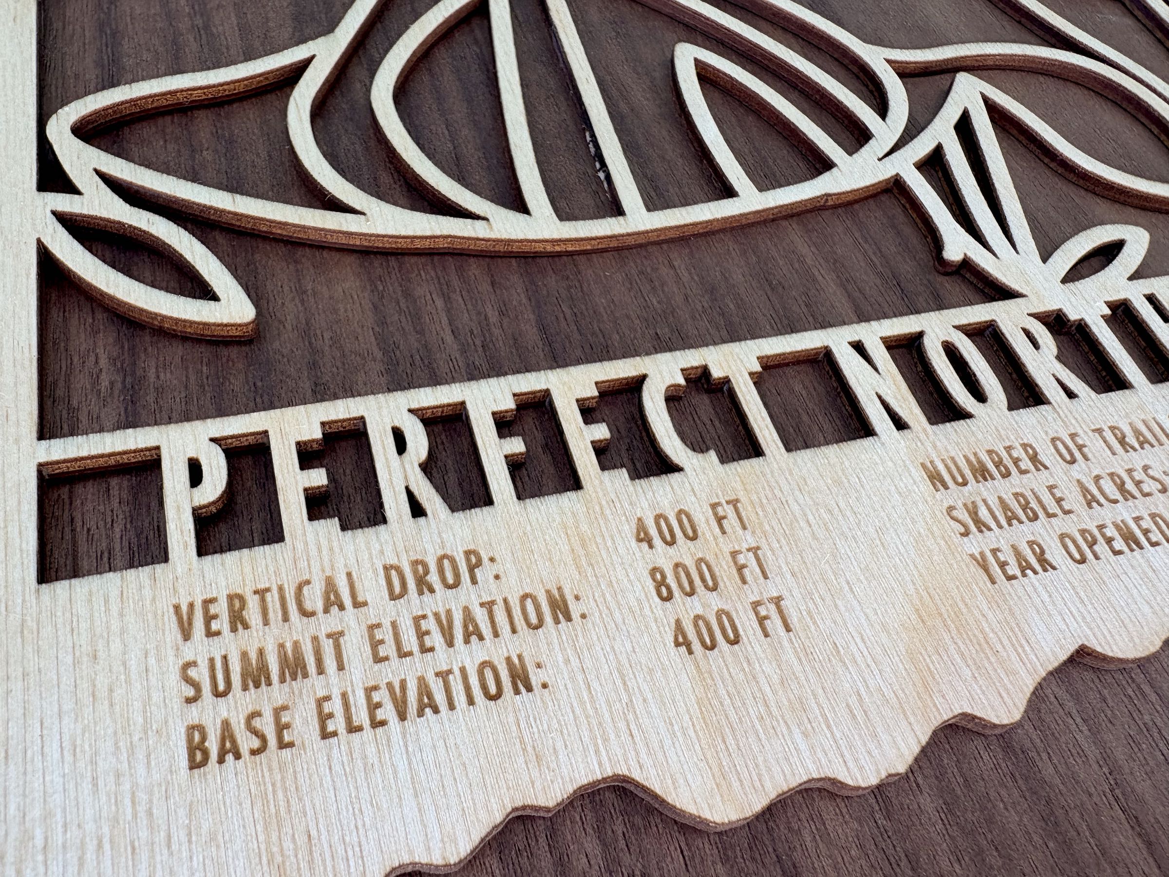 Detailed shot of Perfect North Slopes ski map showing engraved elevation, trail count, and skiable acres on wood decor.