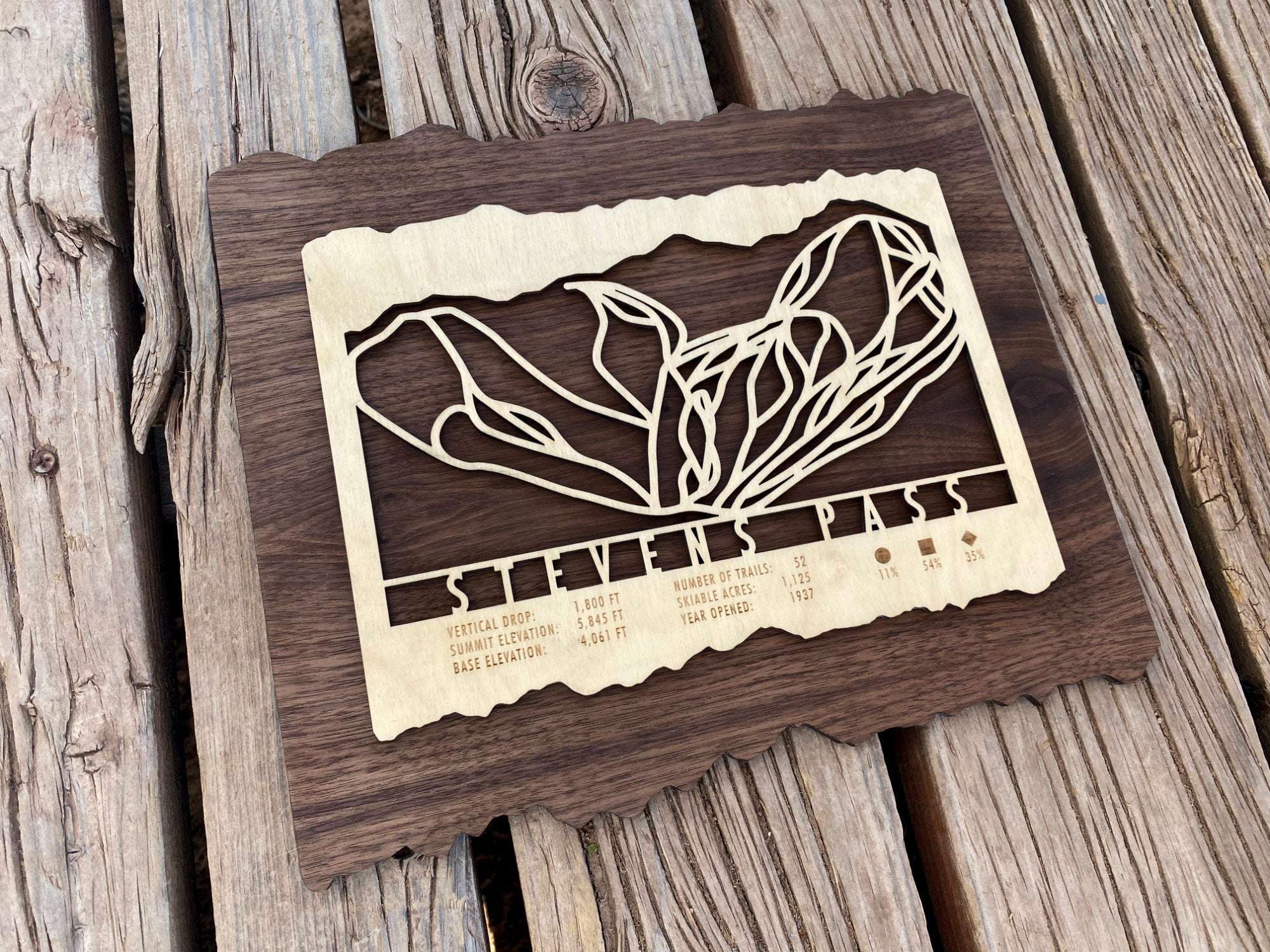 Rustic Stevens Pass Ski Trail Map wood wall art displayed on wooden surface, showcasing intricate ski run design and engraved trail information.