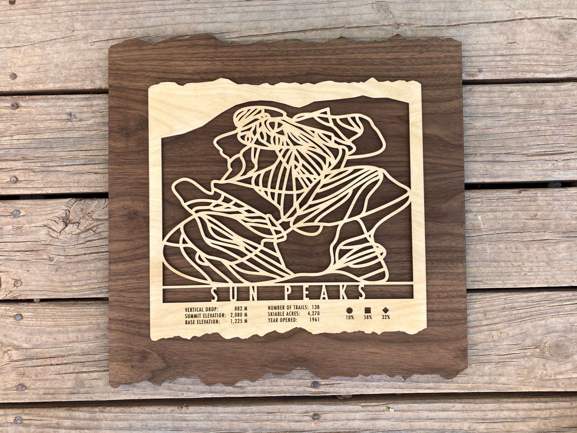 Sun Peaks Ski Trail Map - Wood Wall Decor laid flat on wooden deck, showcasing topographic trail design and engraved resort information.